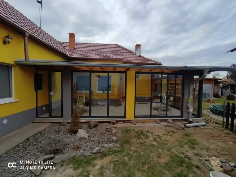 Zasklenie terasy s antracitovou konštrukciou RAL 7016 a posuvným hliníkovým systémom pri žltom dome v Pezinku, pohľad z predu